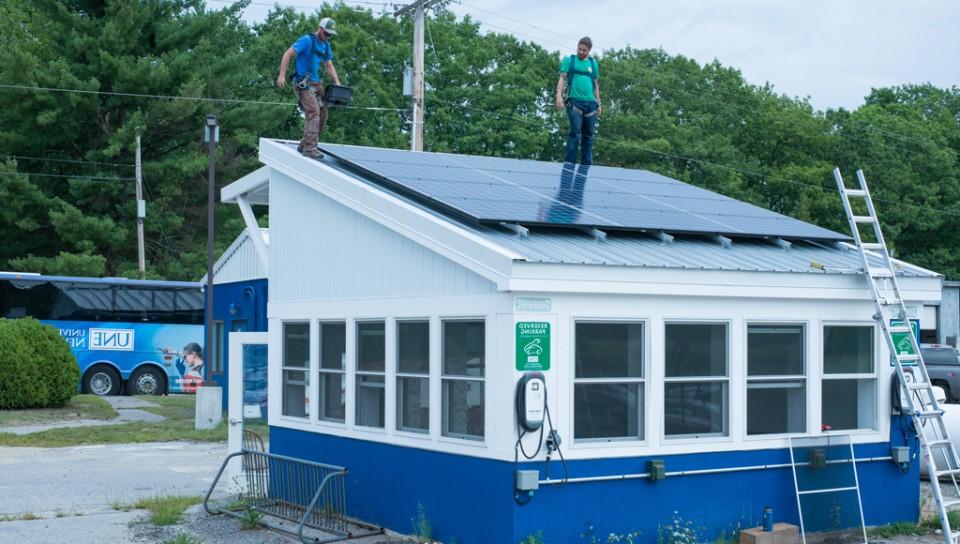 Two workers install solar panels on top of the Bishop Street Lot security building